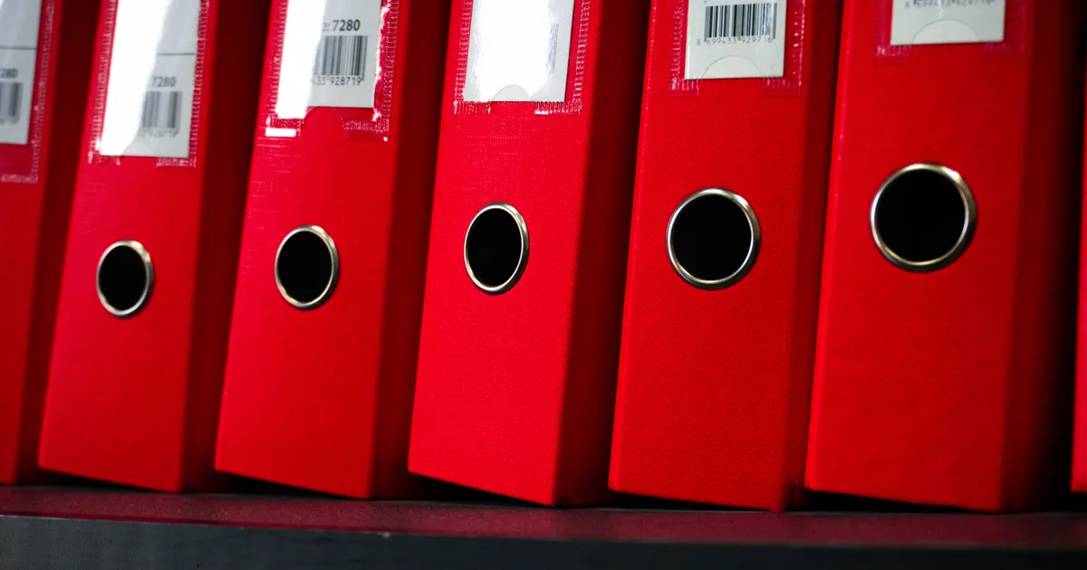 Hilera de carpetas rojas de archivo con etiquetas de código de barras en una estantería
