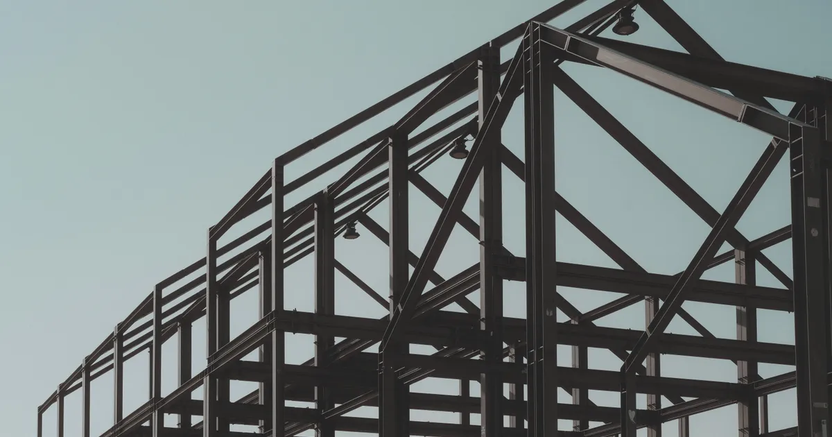 Estructura de acero de una nave industrial en construcción, con sus vigas y lámparas recortadas contra un cielo despejado